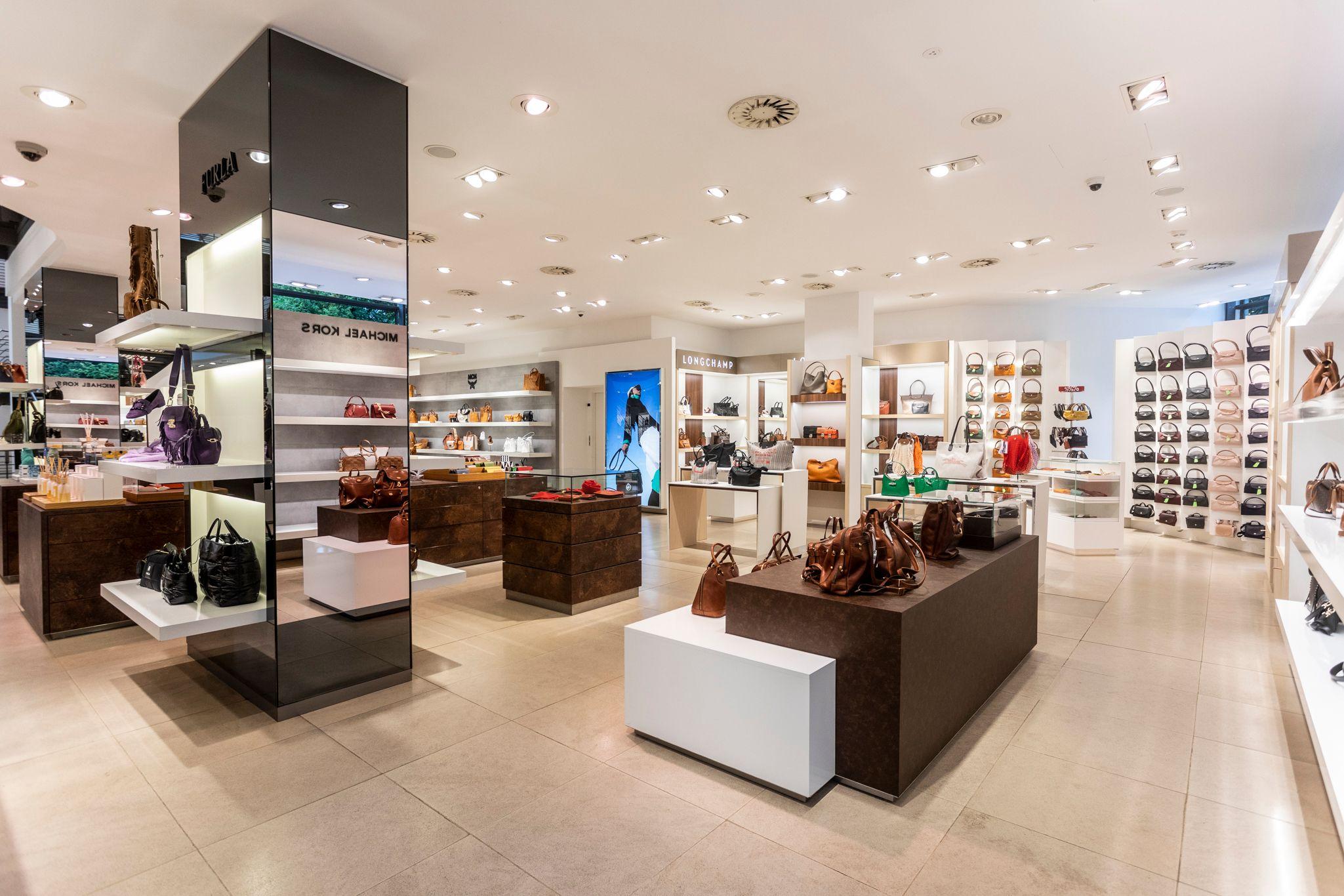 A bright, spacious store interior displaying numerous handbags and shoes on various shelves.