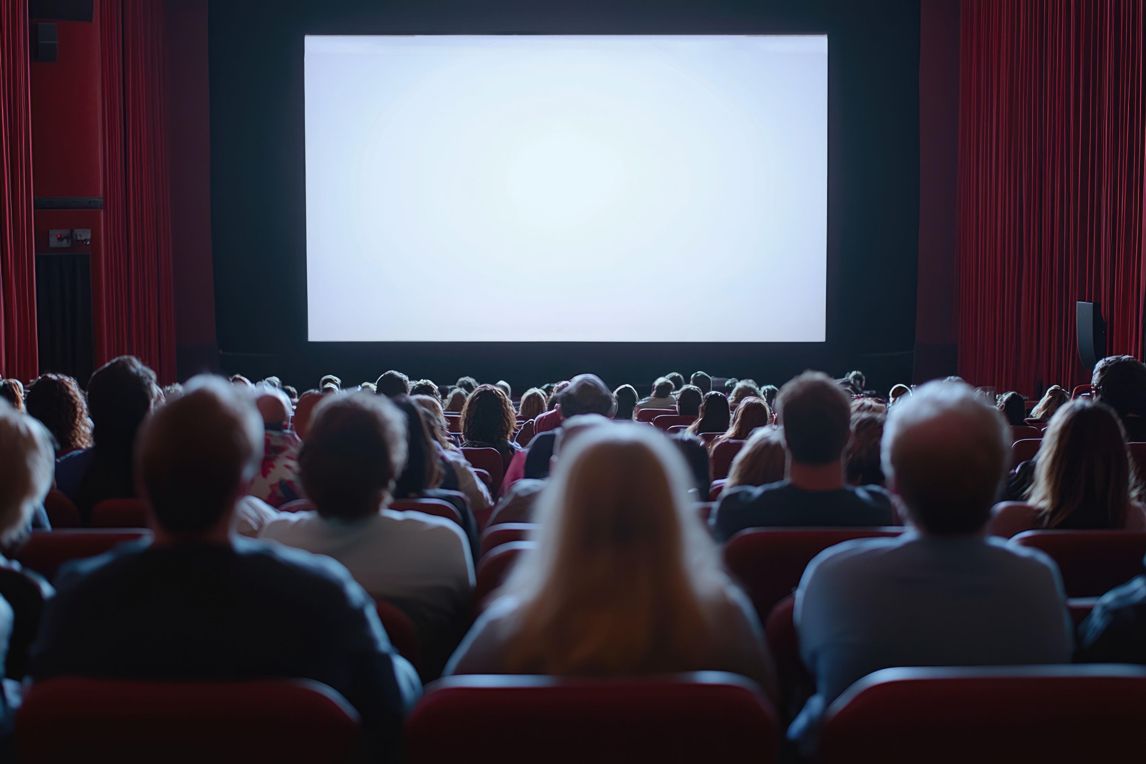 Audience watches a blank screen in a dark movie theater with red seats.