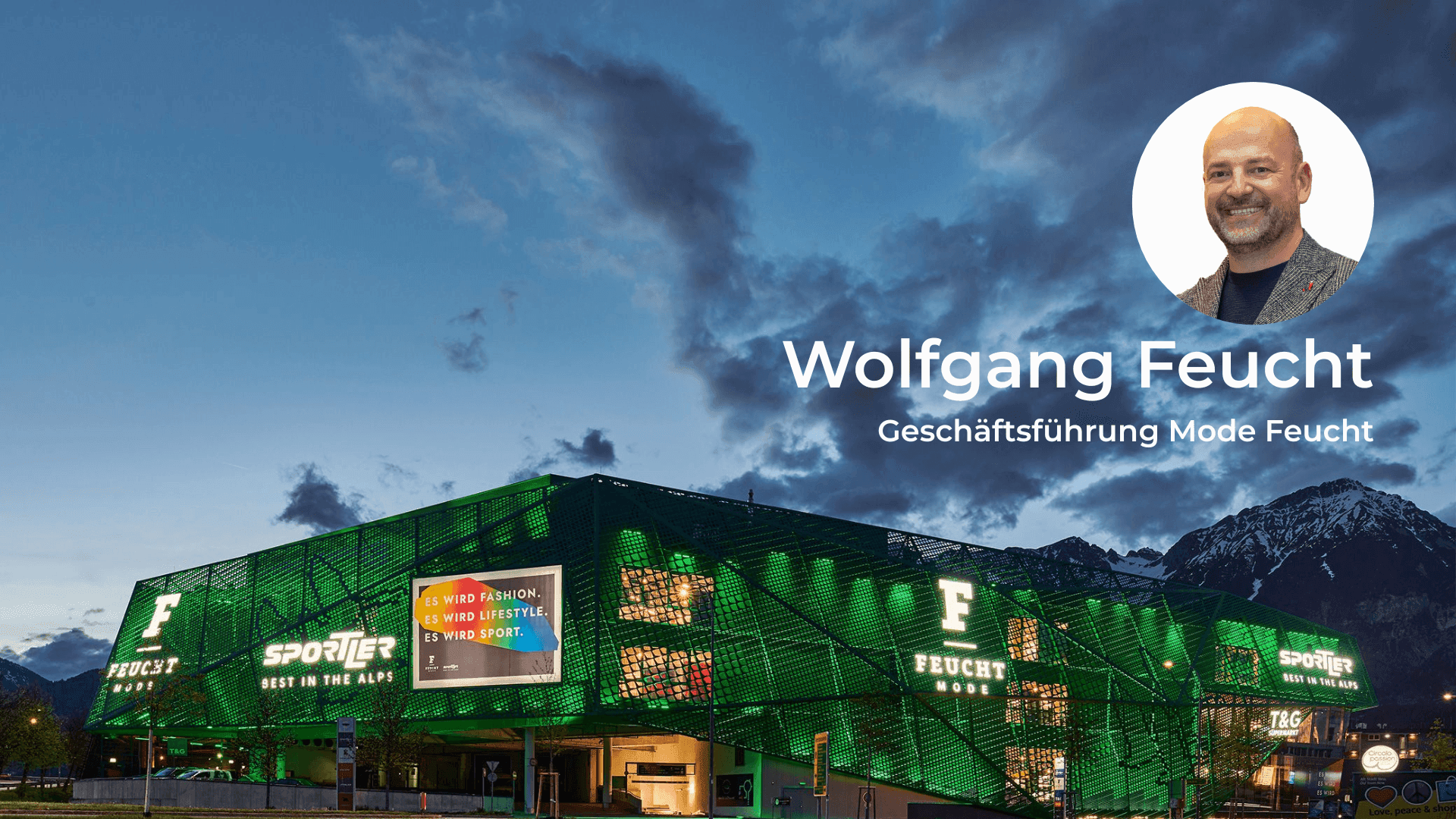 Illuminated green Feucht GmbH building with mountains and Wolfgang Feucht's portrait.