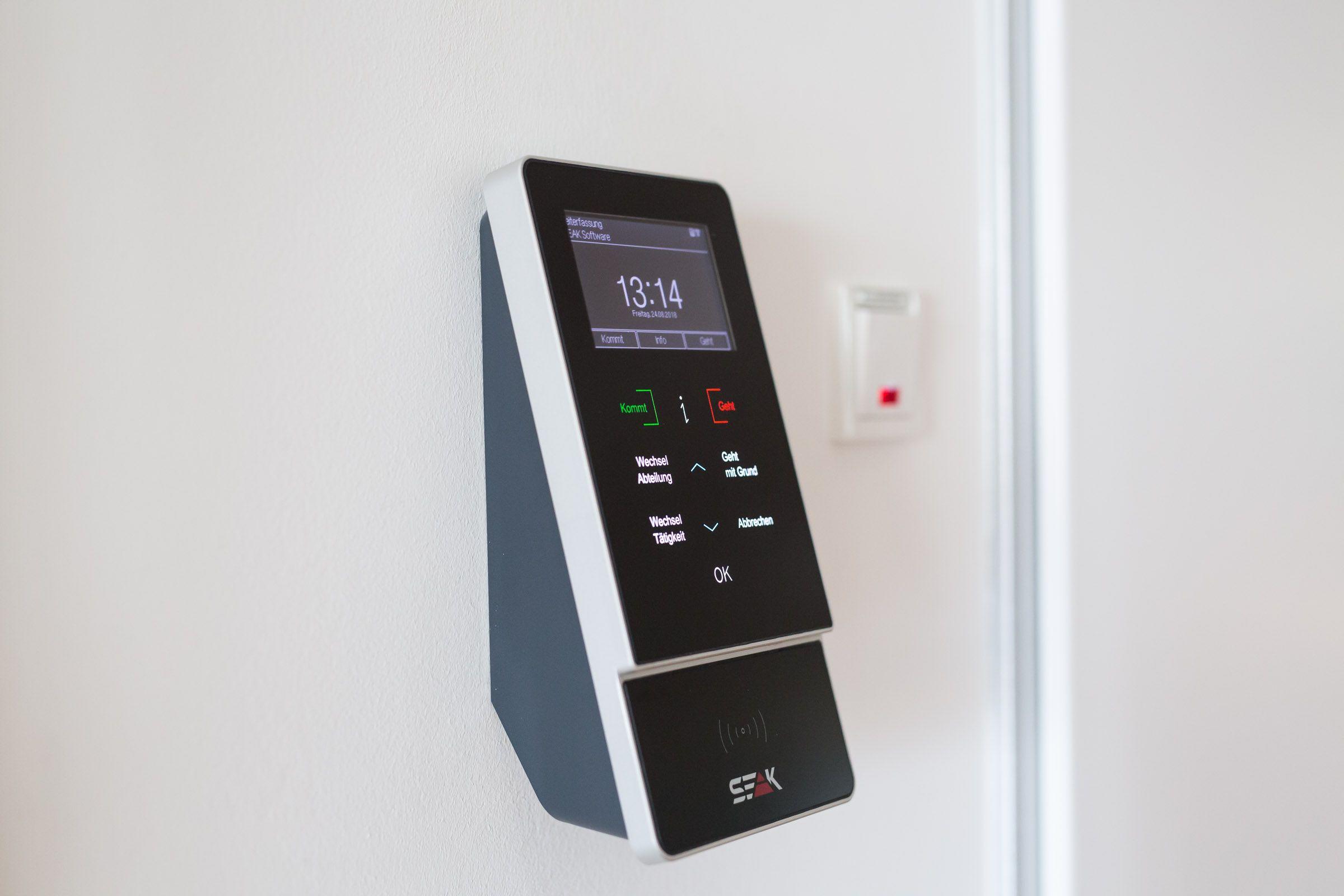 Sleek access control device displaying 12:14 and buttons, mounted on a white wall.