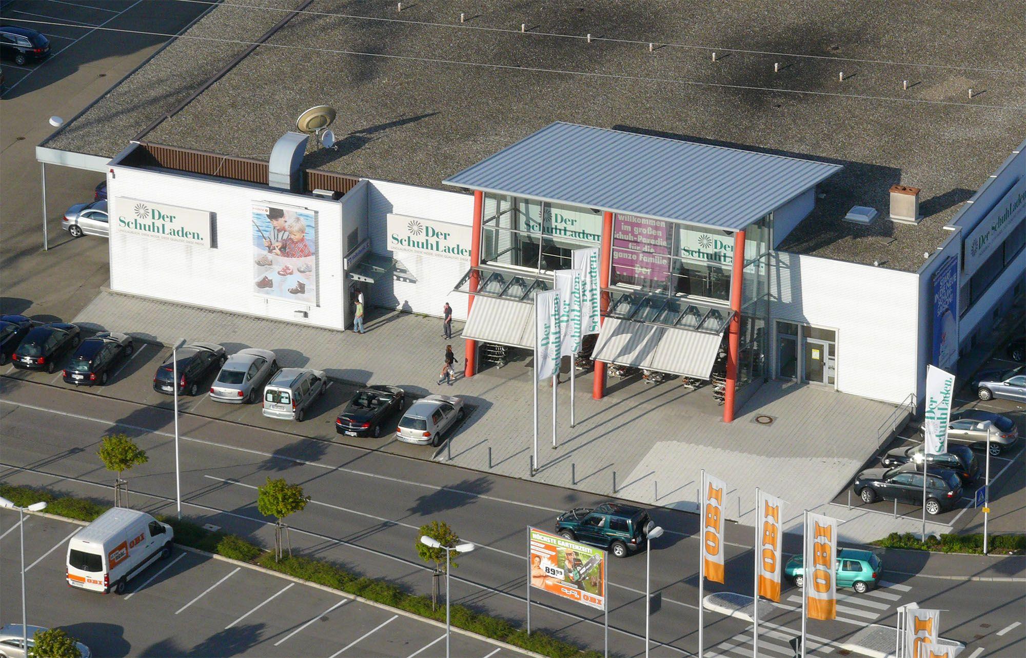 Aerial view of a modern shopping center building with a large parking lot and cars.