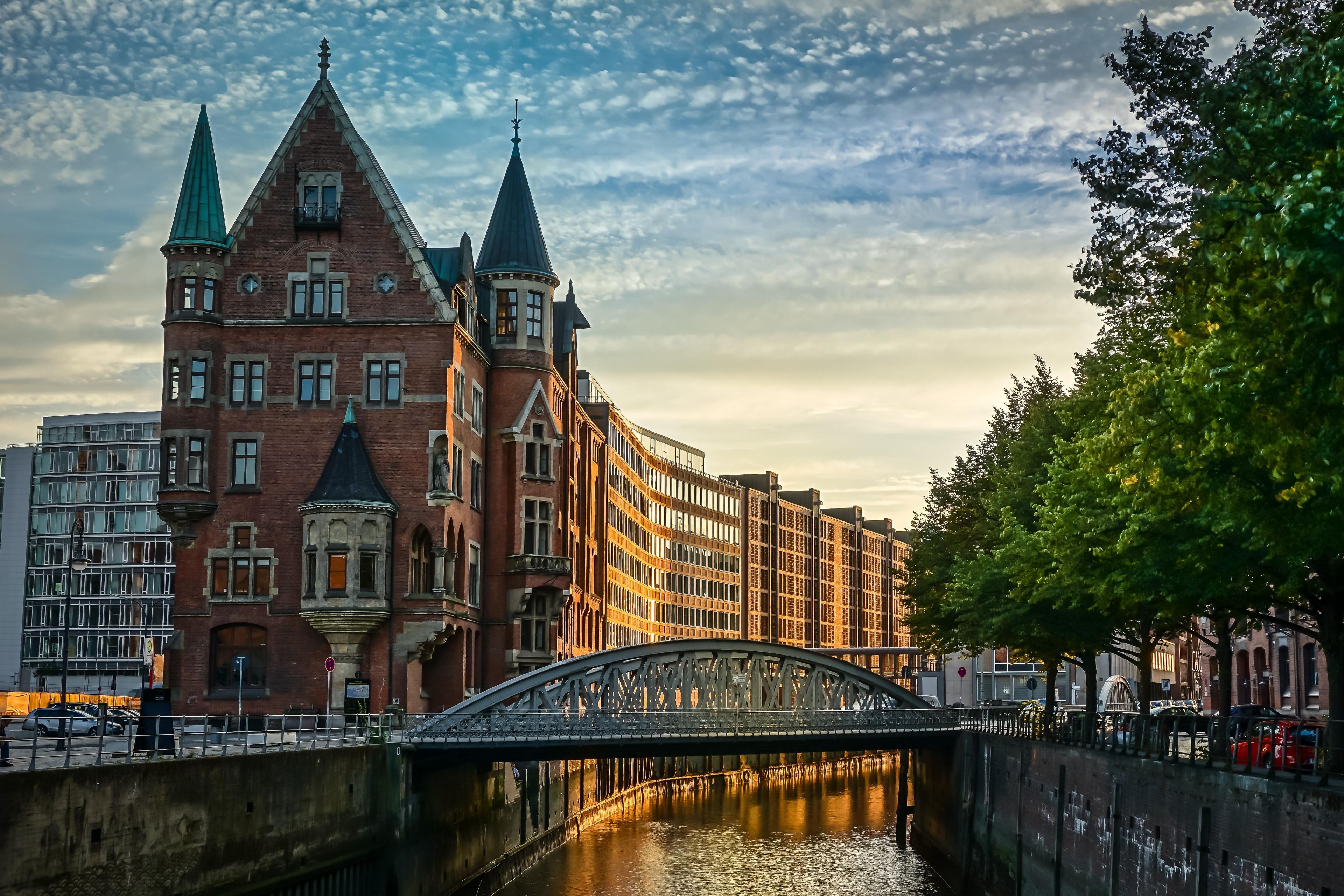 Historic brick building with turrets by a canal and a bridge at sunset.