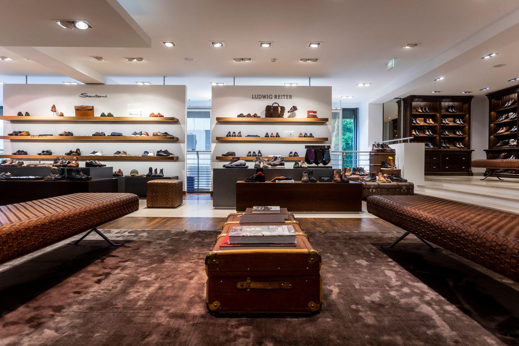 A men's shoe department with shoes on shelves, leather benches, and a central coffee table.