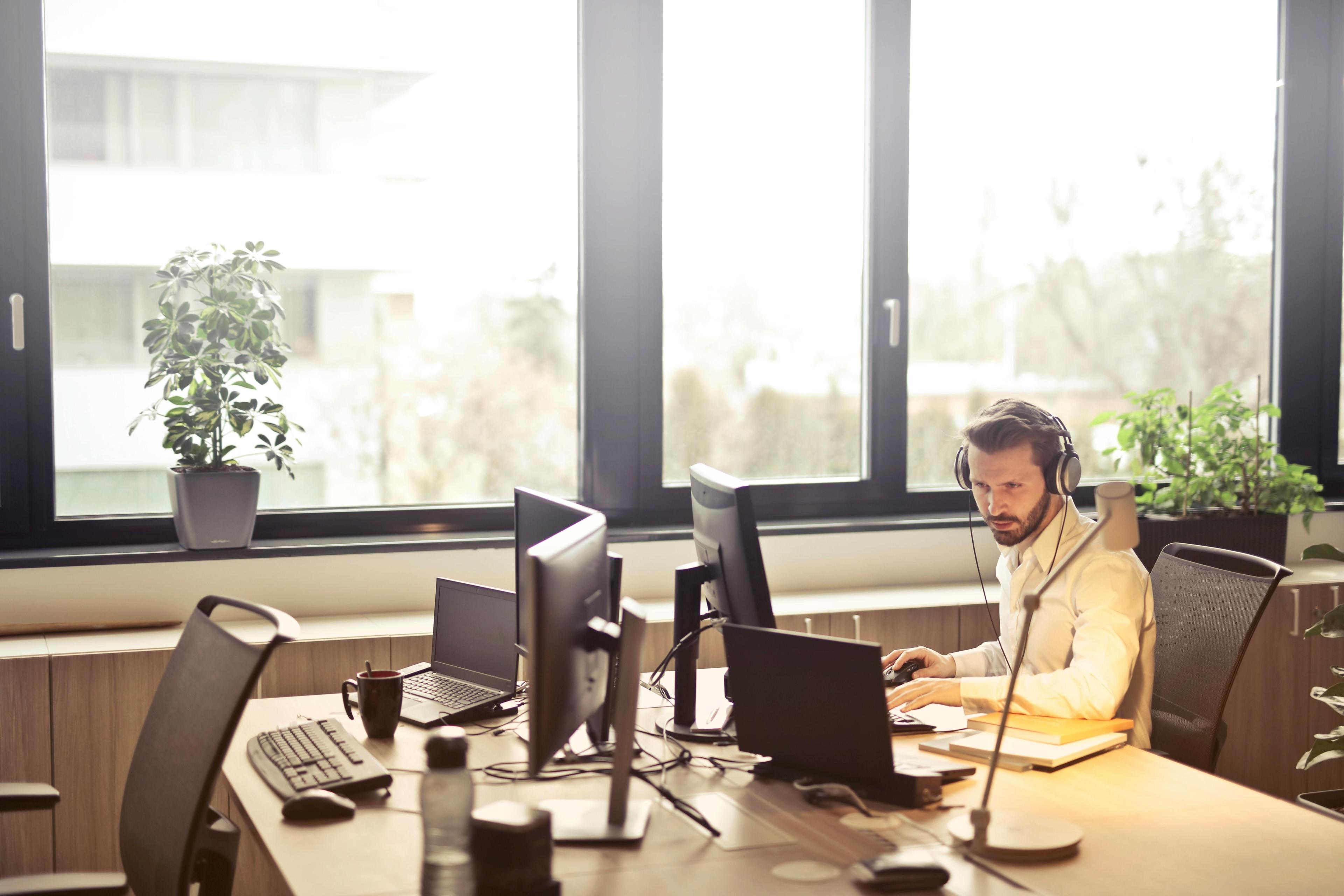 Two women wearing headsets work on laptops at desks in a modern office.