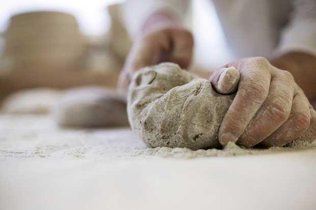 Hands expertly knead a mass of flour-dusted dough on a clean white surface.