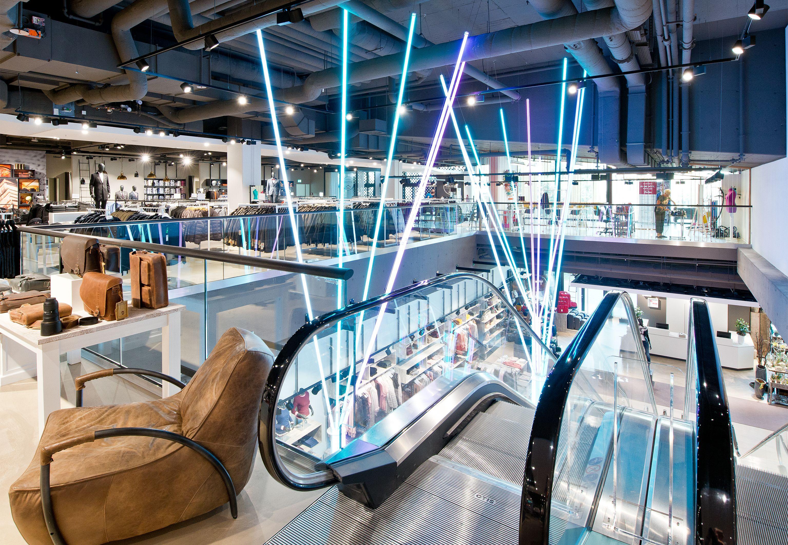 Modern department store interior with escalators and vibrant blue and purple neon lights.
