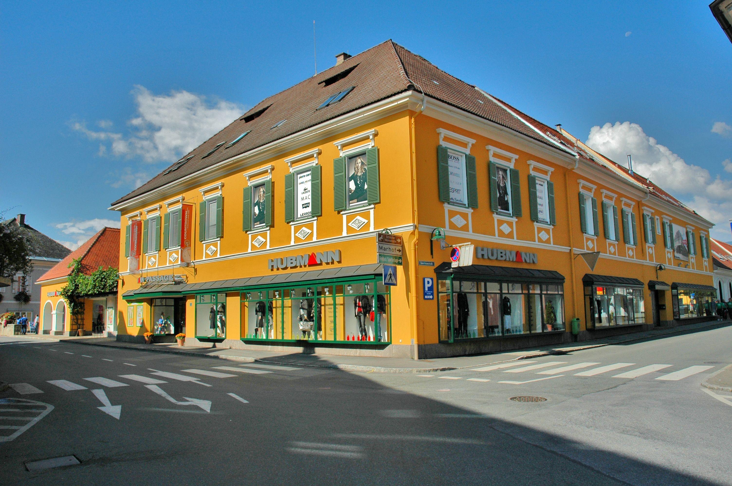 A bright yellow building with green shutters stands at a sunny street corner.