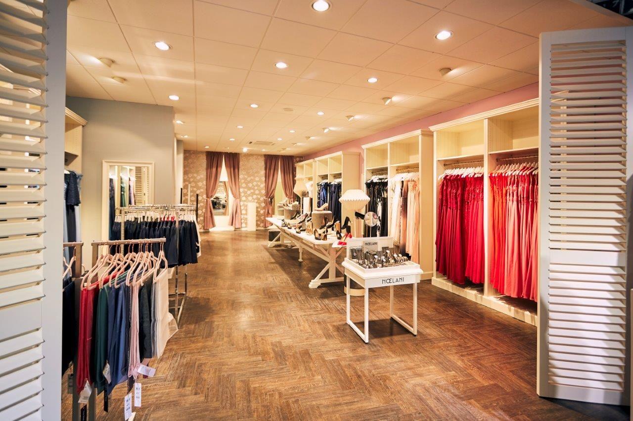 Brightly lit modern boutique interior featuring racks of women's clothing and accessories on display.