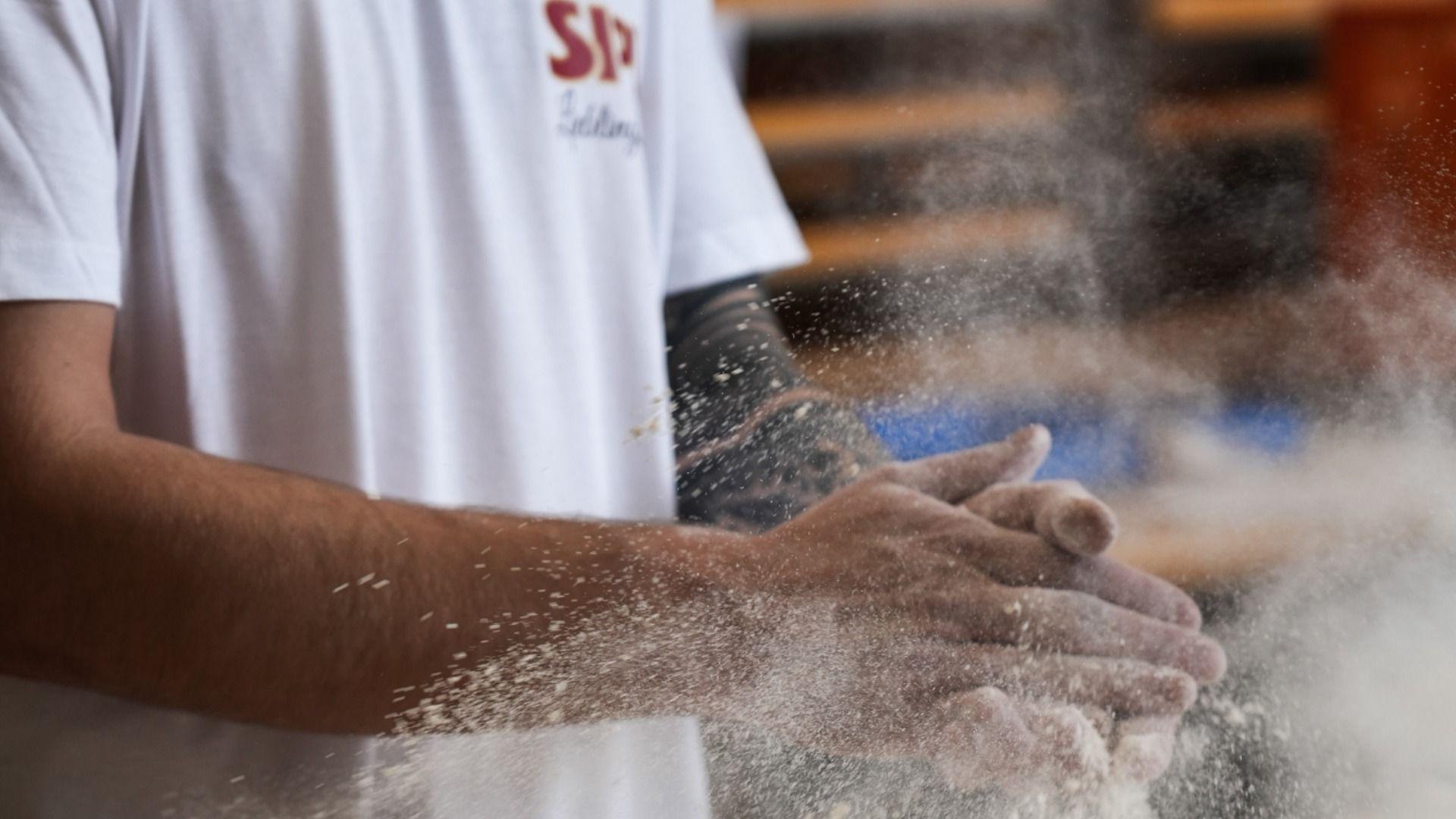 Baker's hands covered in white flour, with a cloud of flour dust rising.