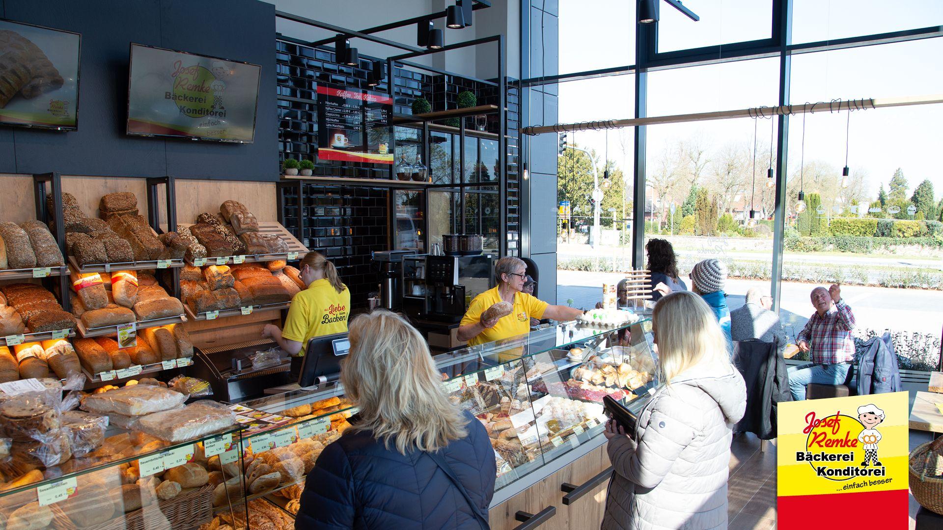 Busy bakery interior with staff serving customers and a large display of fresh baked goods.