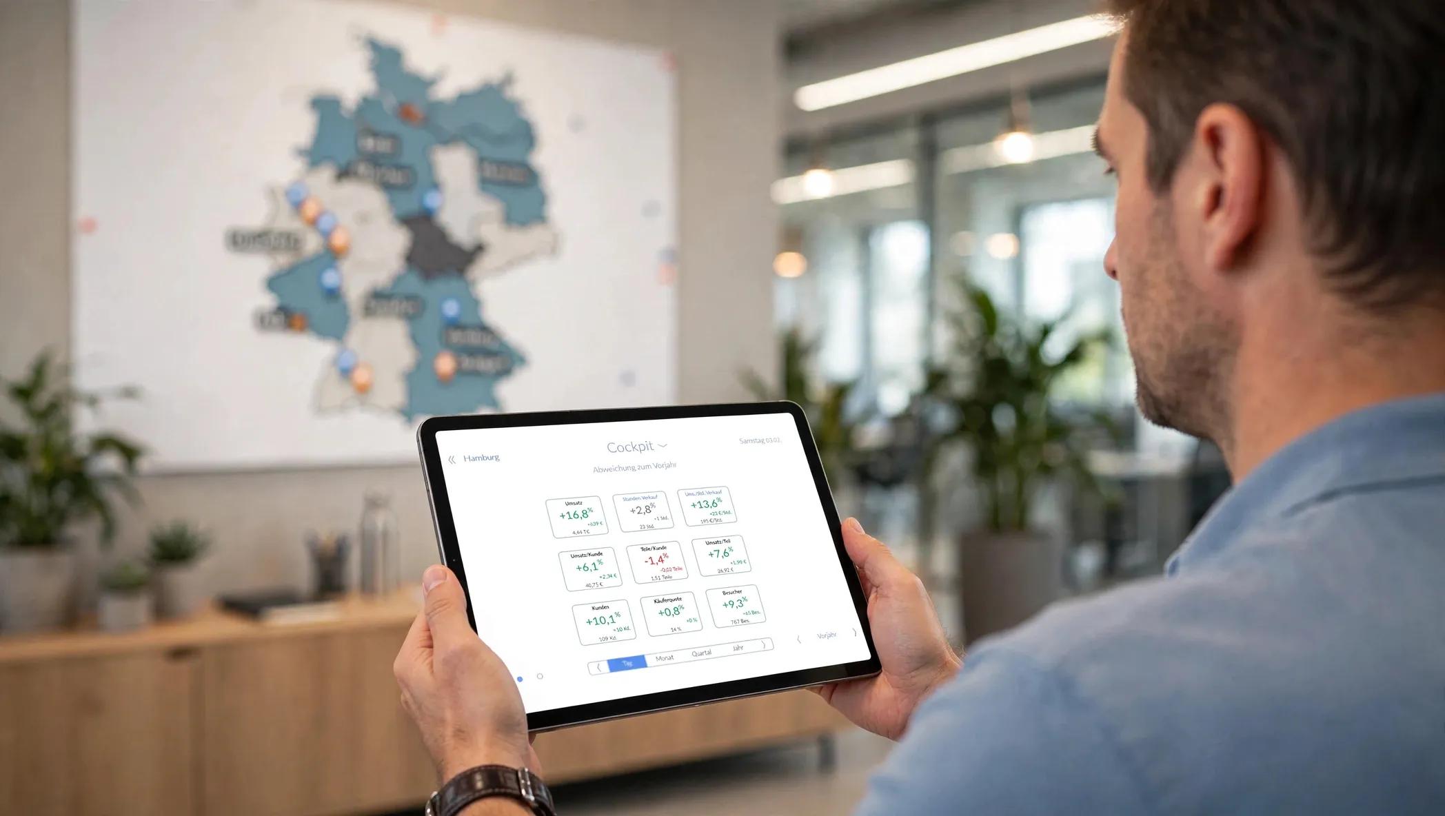 Man views data on tablet in office with large regional map on wall.